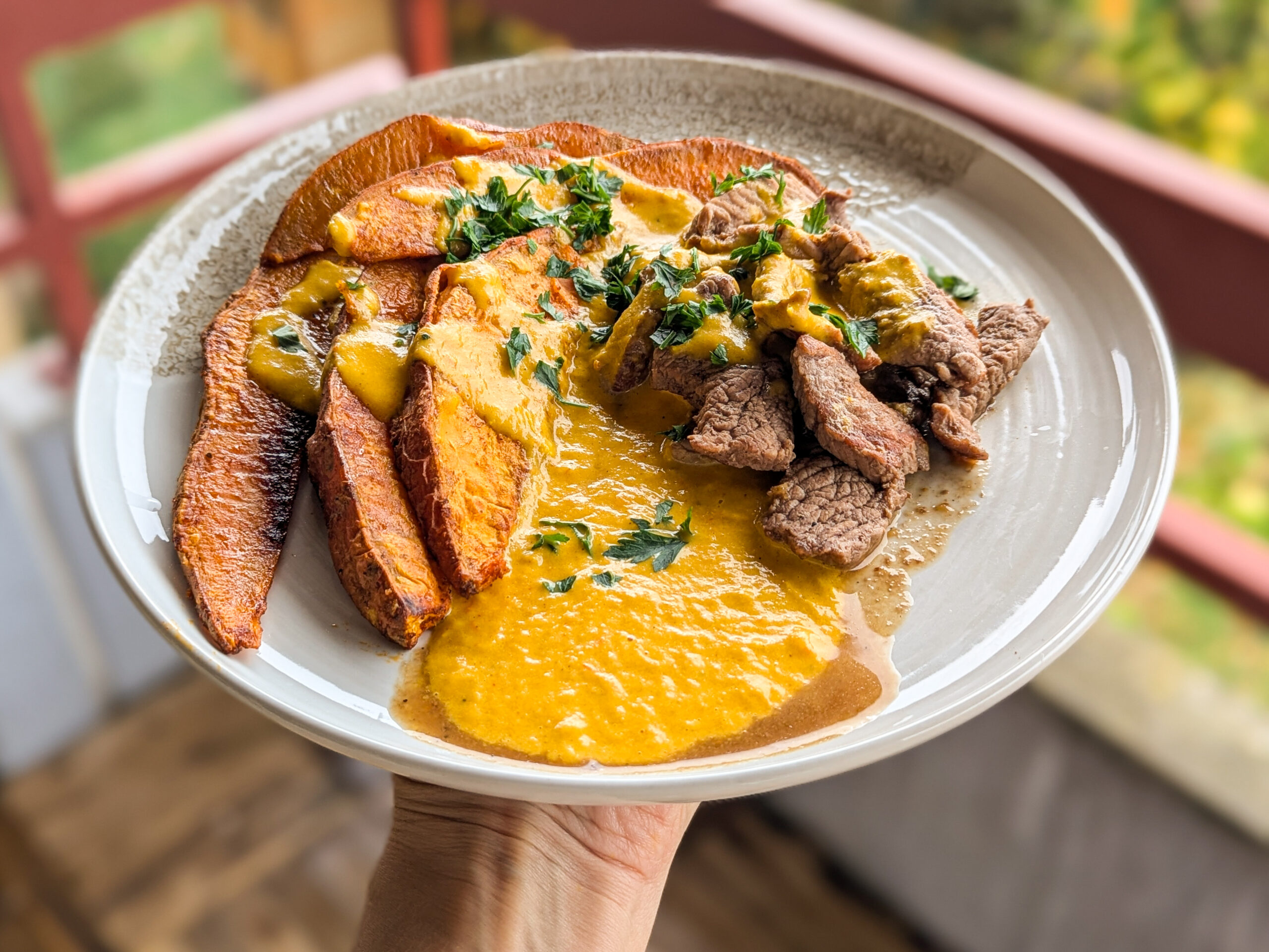 Assiette équilibrée composée de tranches de patate douce rôtie, morceaux de bœuf et sauce crémeuse au poivron et lait de coco, sur fond naturel d’automne.