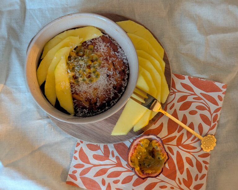 Bol de bowlcake à la farine de coco, accompagné de tranches de mangue fraîche et d’un demi-fruit de la passion, sur une serviette orange à motifs feuillus.