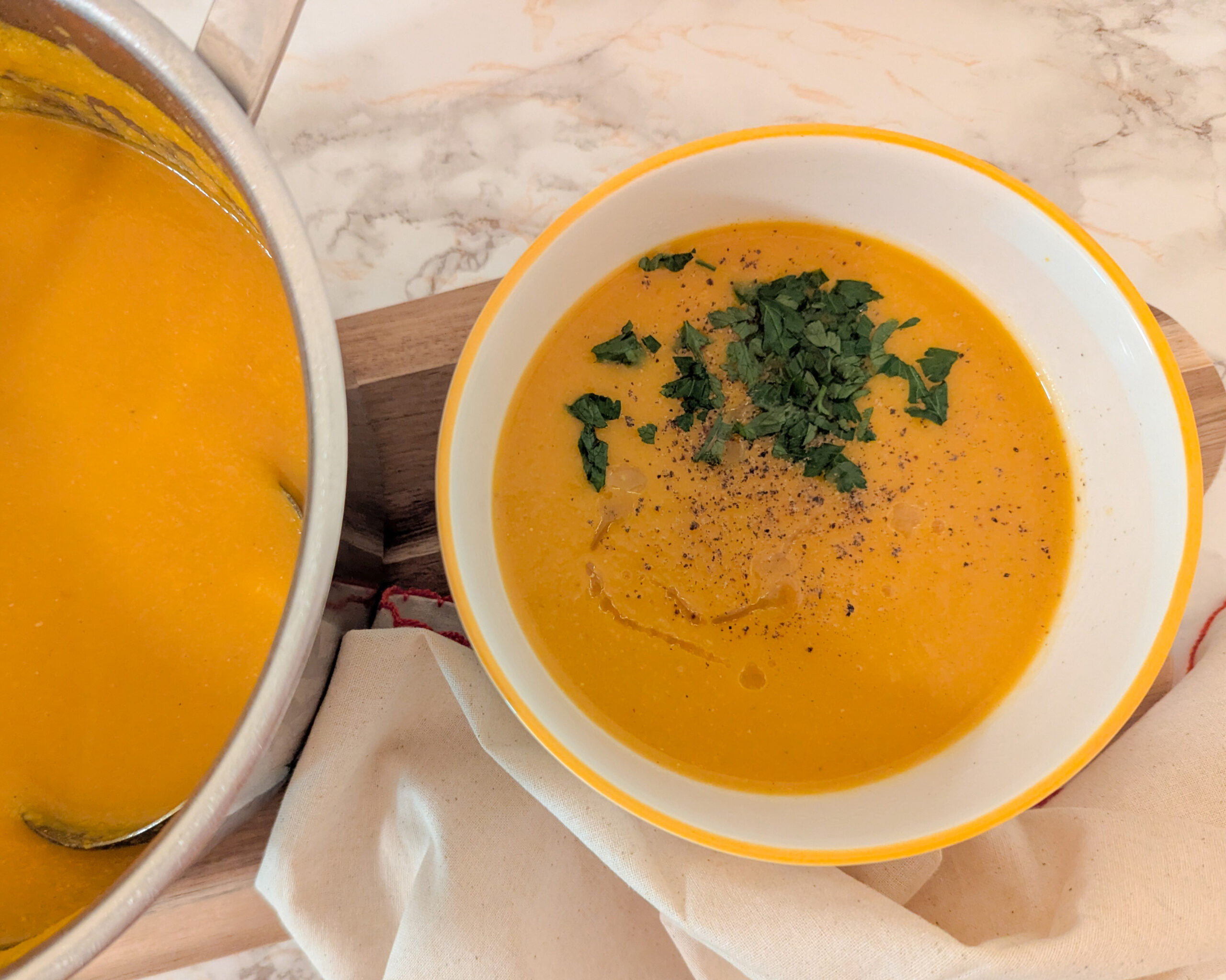 Bol de velouté de carottes et lentilles corail, garni de persil plat frais et d’un filet d’huile d’olive, posé sur une nappe naturelle.
