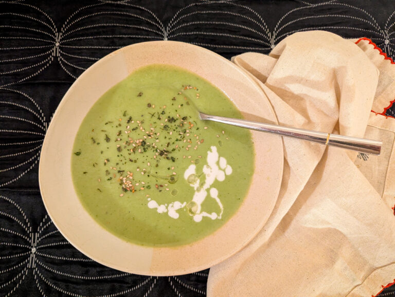 Bol de velouté vert au brocoli avec un filet de lait de coco, herbes et épices, servi avec une cuillère sur une serviette claire.
