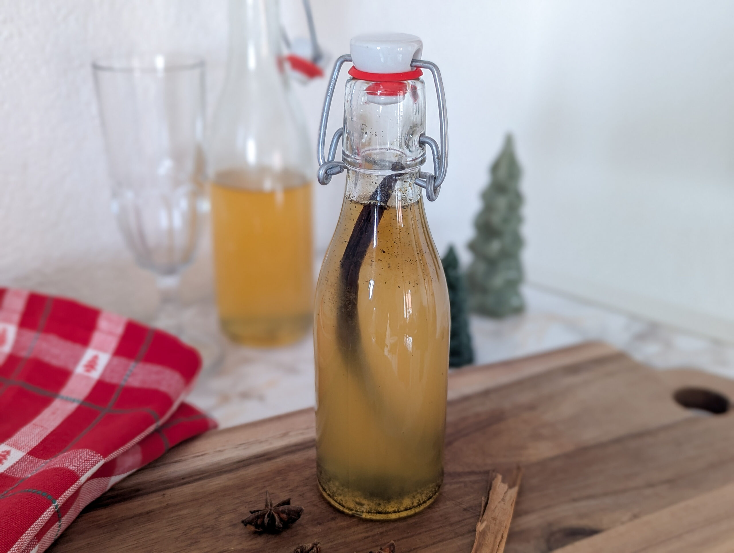 Bouteille de sirop aux épices de Noël maison, à base d’orange, de cannelle et de vanille, posée sur une planche en bois dans une ambiance chaleureuse.